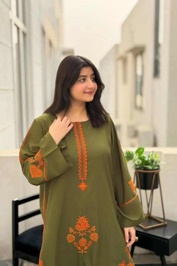 Woman wearing a green dress with orange embroidery indoors