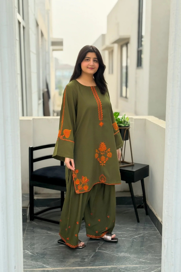 Woman wearing a green traditional outfit with orange patterns in an indoor setting.