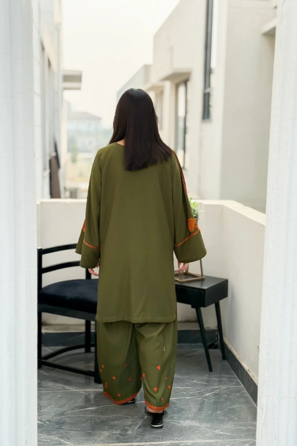 Woman in a green outfit walking away from the camera in an indoor setting.