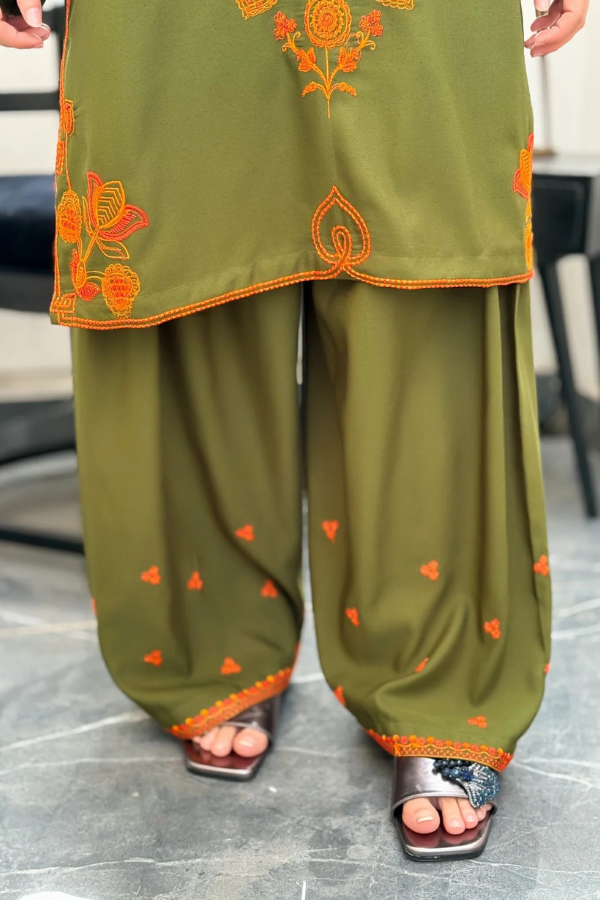 Green traditional outfit with orange embroidery on a gray floor.