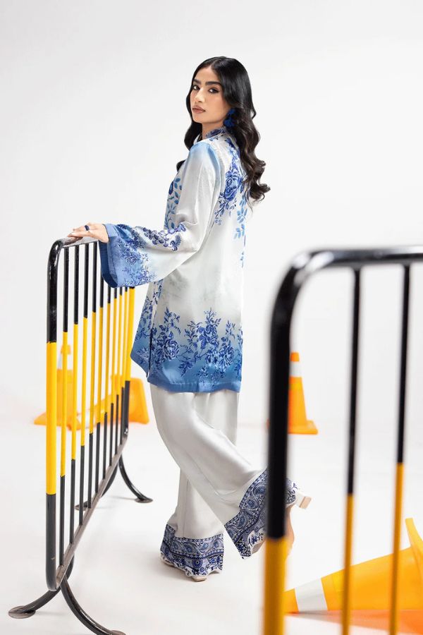 Woman in a white and blue traditional outfit standing next to a decorative metal railing.