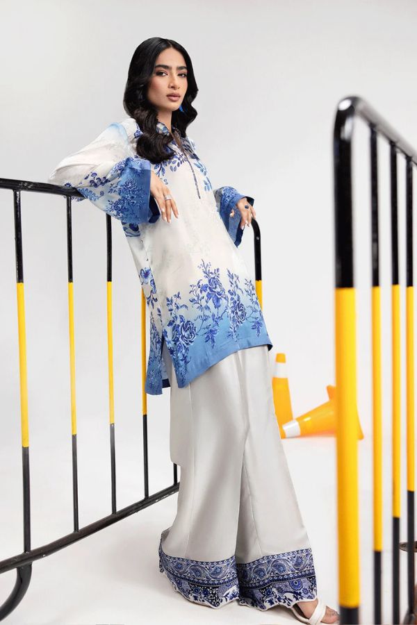 Woman wearing a white and blue traditional outfit with floral patterns, standing against a white background.
