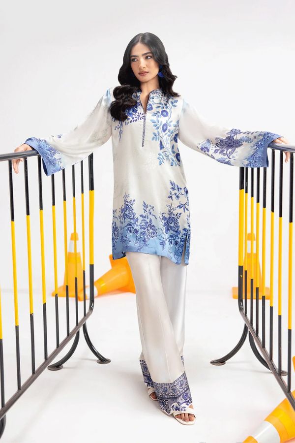 Woman wearing a white outfit with blue floral patterns standing next to a crib.