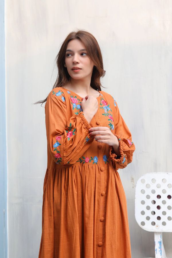 Woman wearing an orange dress with floral embroidery against a light background