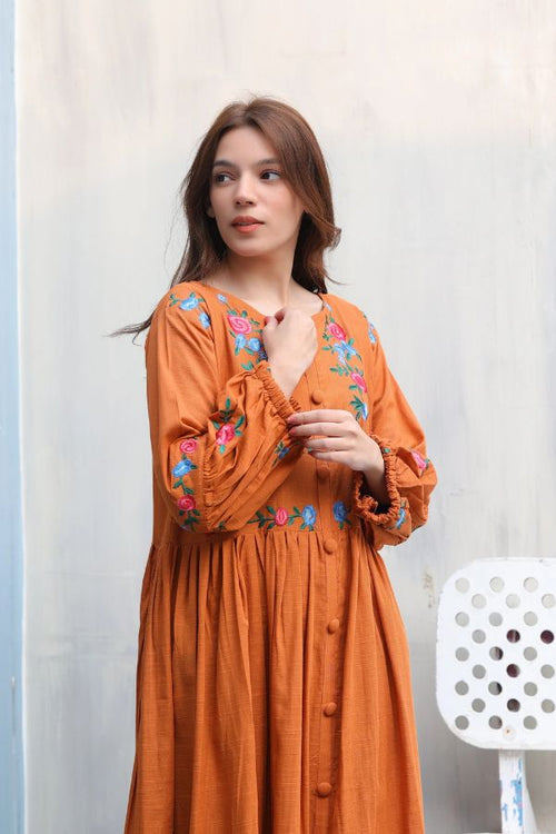 Woman wearing an orange dress with floral embroidery against a light background