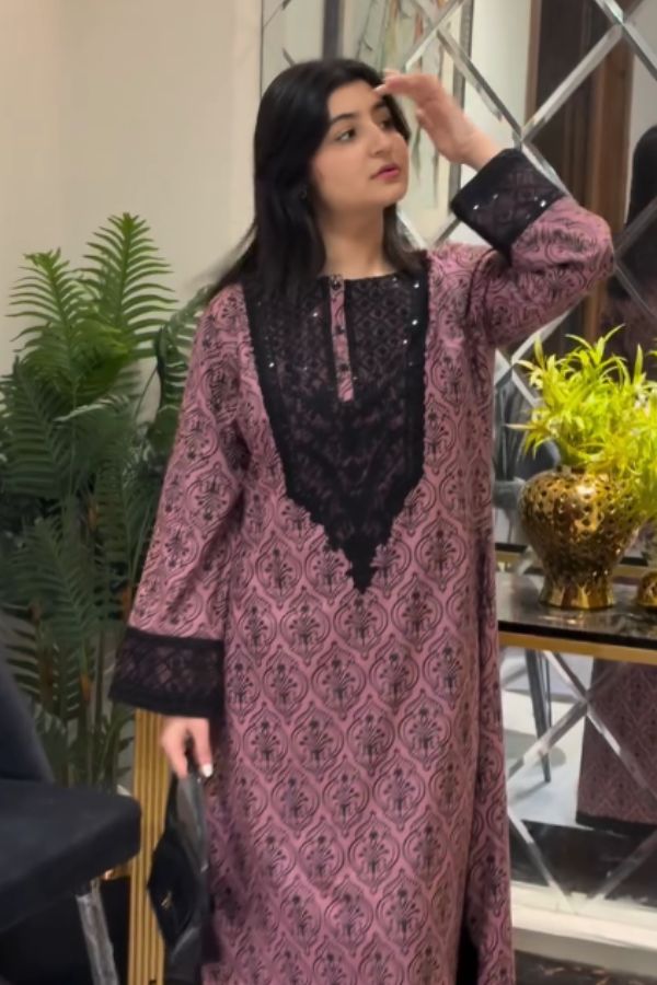 Woman wearing a pink and black patterned dress indoors with plants and decor in the background