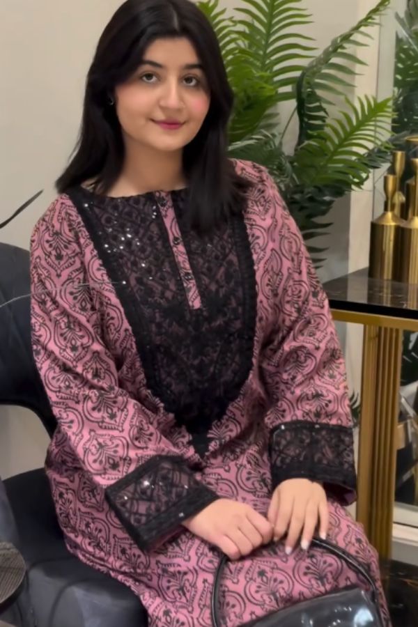 Woman wearing a pink and black patterned outfit sitting indoors with plants in the background