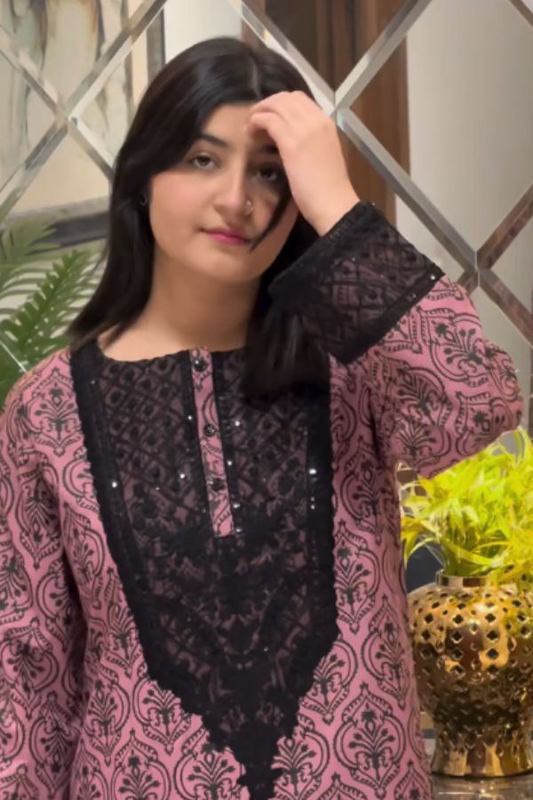 Woman wearing a pink and black patterned outfit with a decorative headpiece indoors.