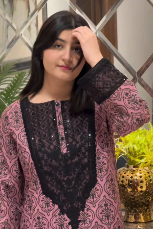 Woman wearing a pink and black patterned outfit with a decorative headpiece indoors.