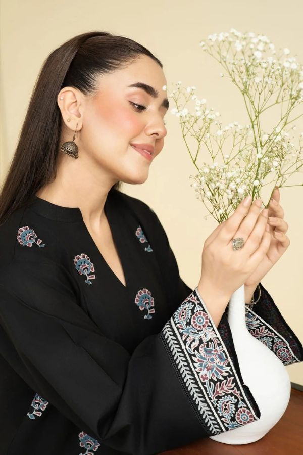 Woman holding a small bouquet of flowers, wearing a black embroidered outfit.