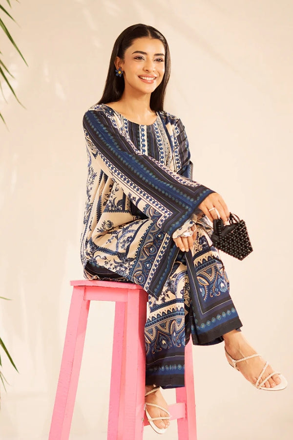 Woman in a patterned outfit sitting on a pink stool against a plain background