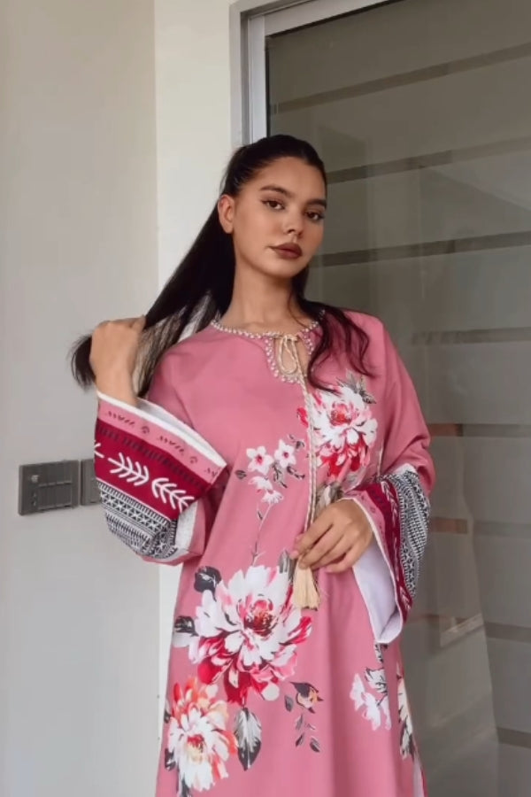 Woman wearing a pink floral dress with a patterned shawl, standing indoors.