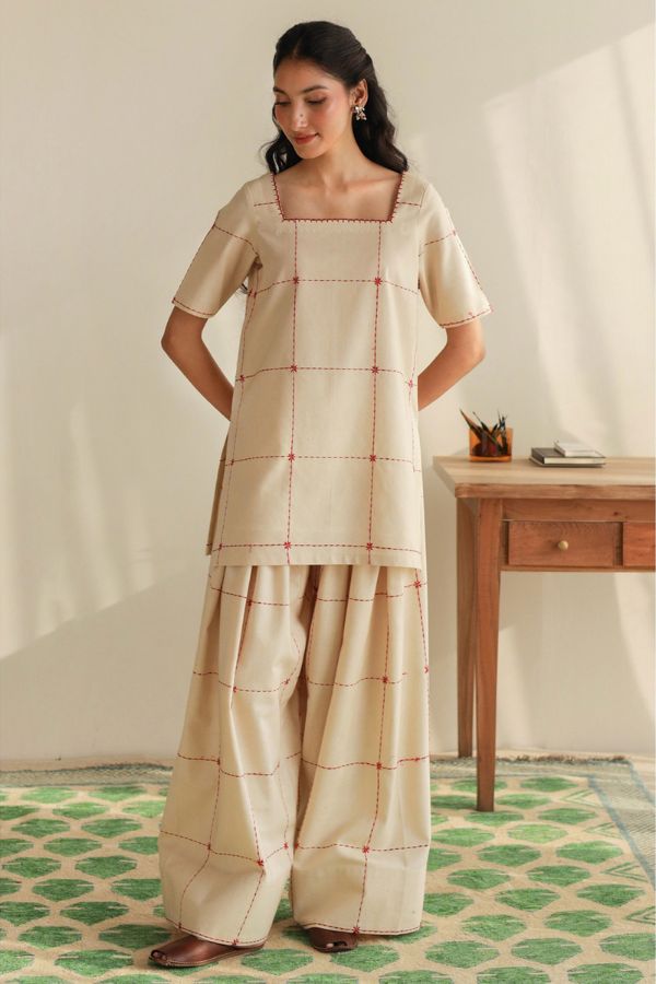 Woman wearing a traditional outfit with a checkered pattern in a room with a wooden table and green and white patterned floor.