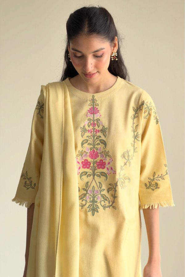 Woman wearing a light yellow kurta with floral embroidery on a plain background