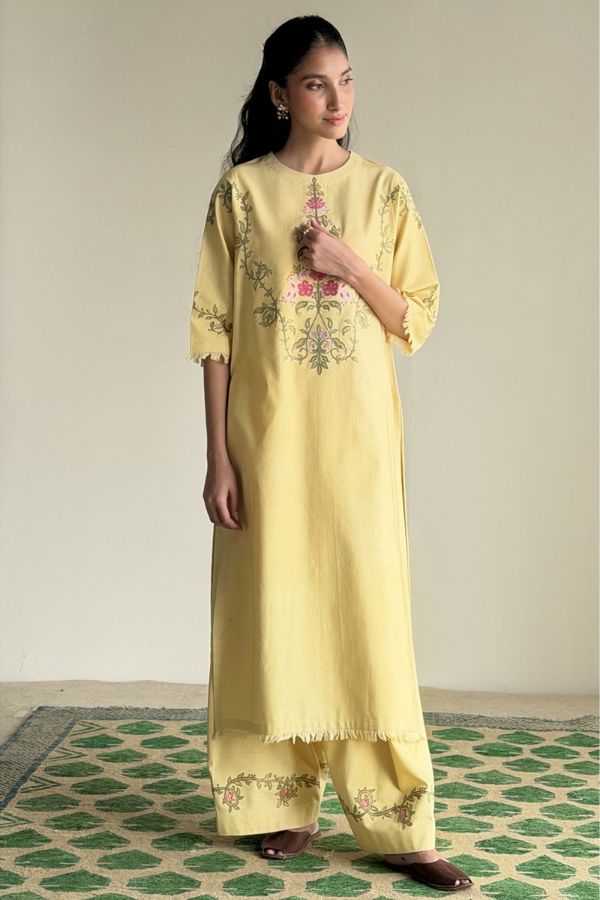 Woman wearing a yellow embroidered outfit on a patterned rug.