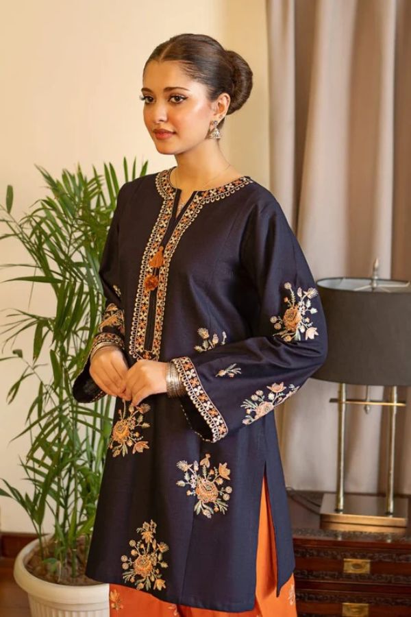 Woman wearing a dark blue embroidered outfit with an orange bottom in a room setting.