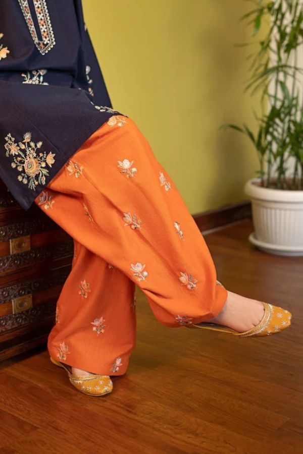 Person wearing orange pants with floral patterns on a wooden floor.