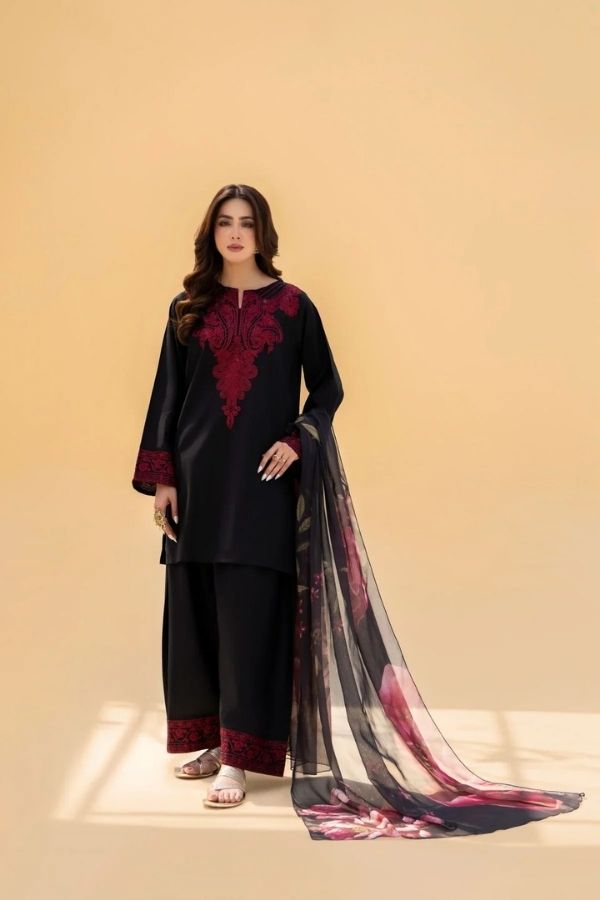 Woman wearing a black and red embroidered outfit with a sheer dupatta on a beige background
