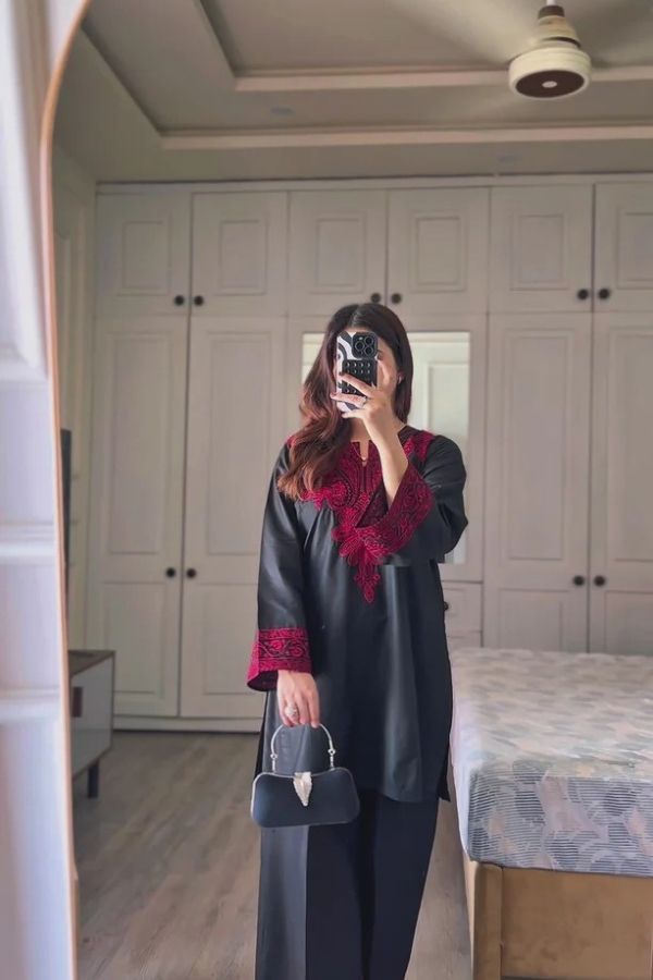 Person taking a mirror selfie in a room with white wardrobes and a bed.