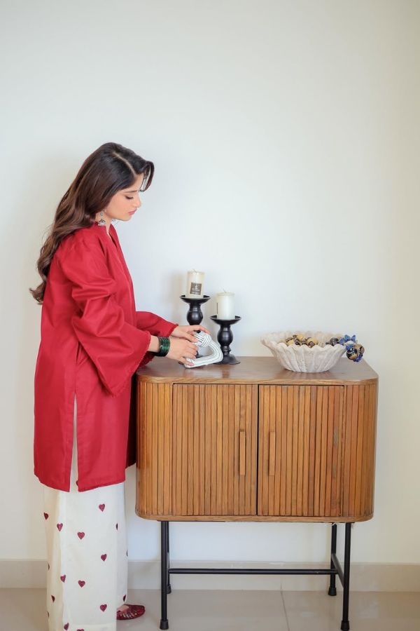 Woman in a red coat standing next to a wooden side table with decorative items.