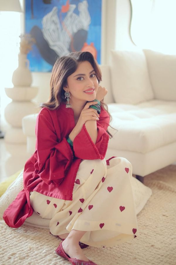 Woman in a red top and white pants with heart patterns sitting on a couch.