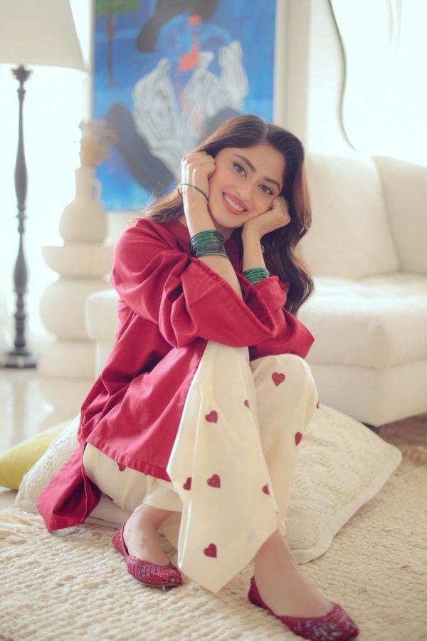Woman in a red sweater and white pants with heart patterns sitting on a couch.