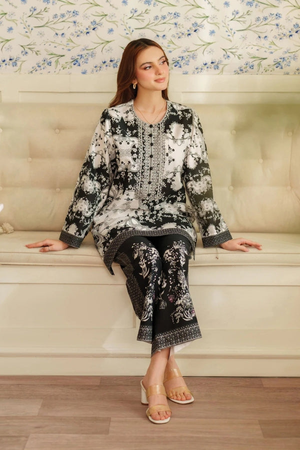 Woman sitting on a couch wearing a black and white floral outfit with a decorative pattern.