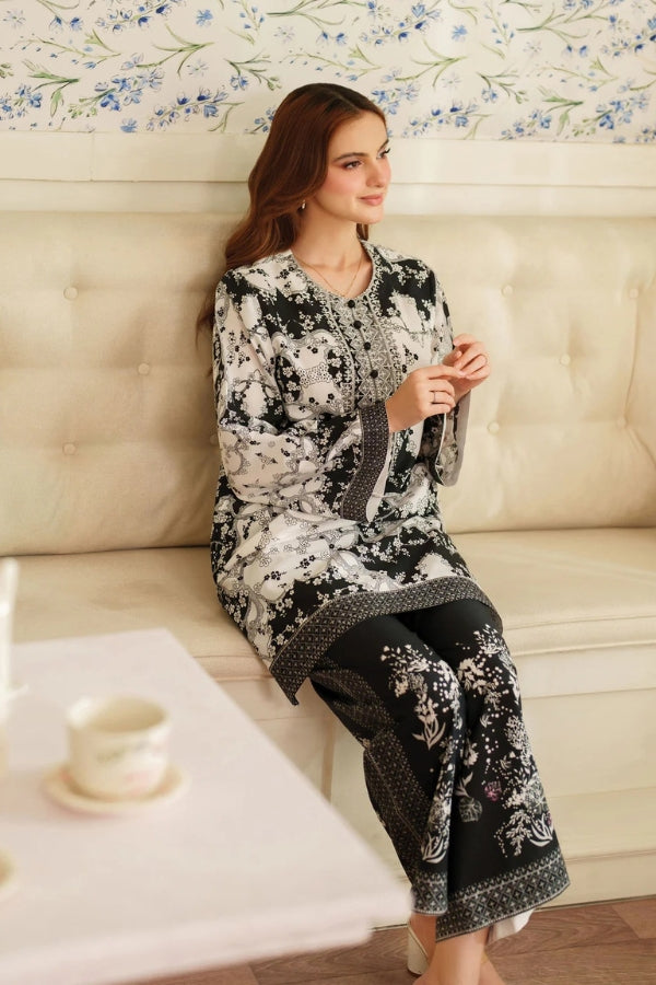 Woman in a black and white patterned outfit sitting on a beige sofa with floral wallpaper.