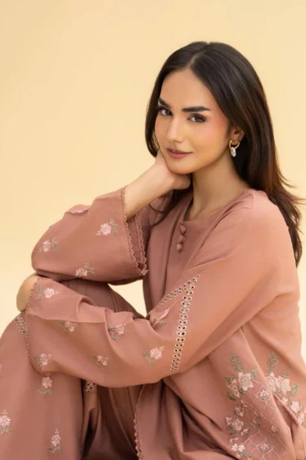 Woman wearing a pink embroidered outfit against a beige background