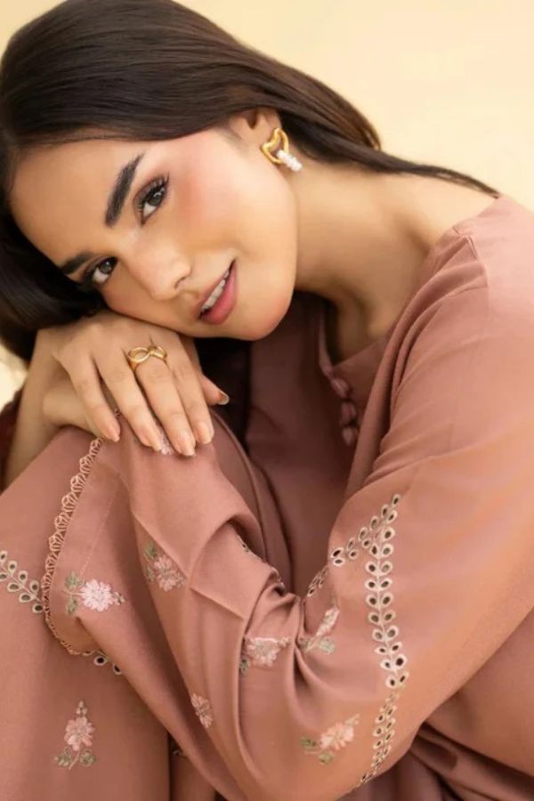 Woman wearing a brown embroidered outfit with a neutral background