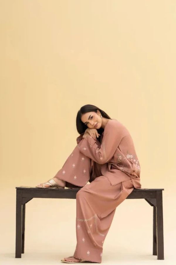 Woman in a pink outfit sitting on a bench against a beige background