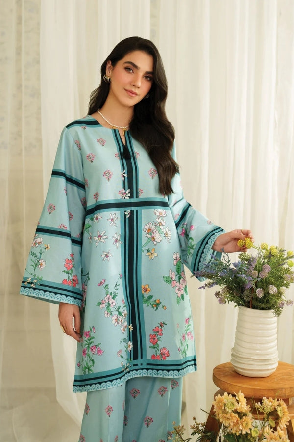 Woman wearing a light blue embroidered outfit with a white curtain background