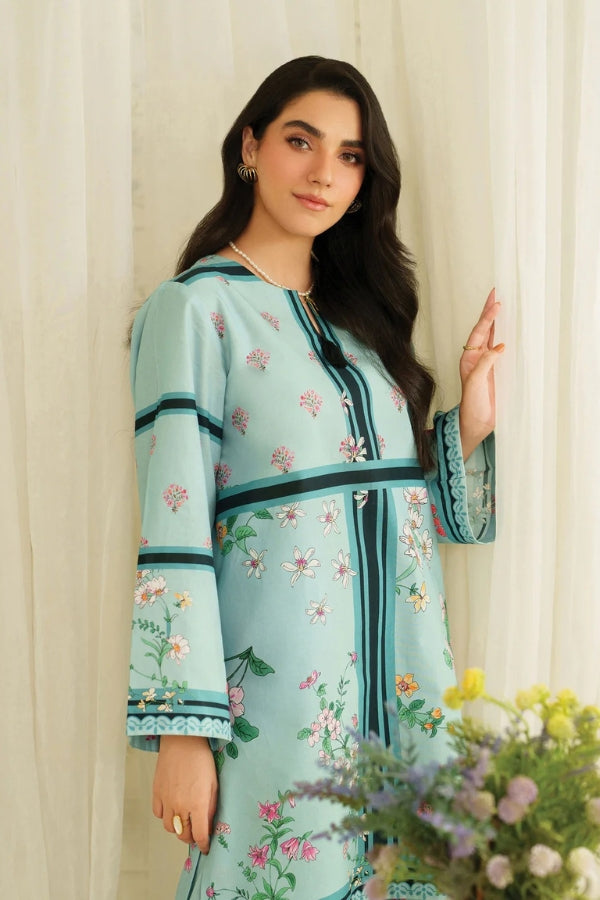 Woman wearing a light blue floral dress standing in front of a white curtain with flowers in the foreground.