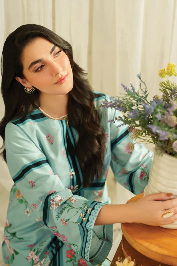 Woman in a light blue embroidered outfit sitting at a table with flowers.