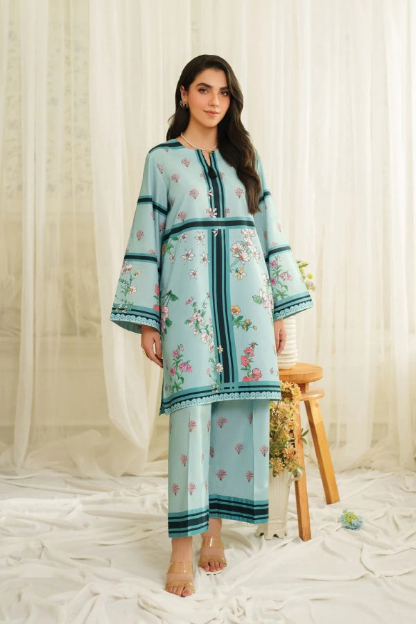 Woman wearing a light blue embroidered outfit with floral patterns against a white curtain background.