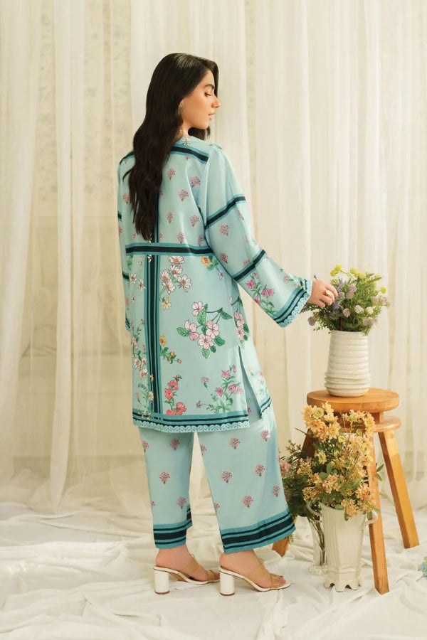 Woman in a light blue floral outfit holding a vase with flowers against a white curtain background.