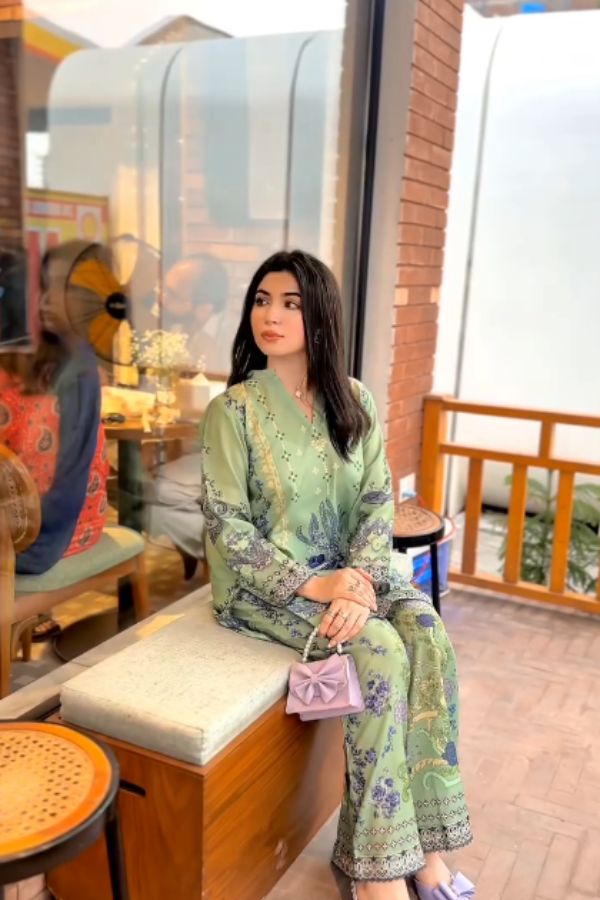 Woman in a green floral outfit sitting on a bench with a pink handbag.
