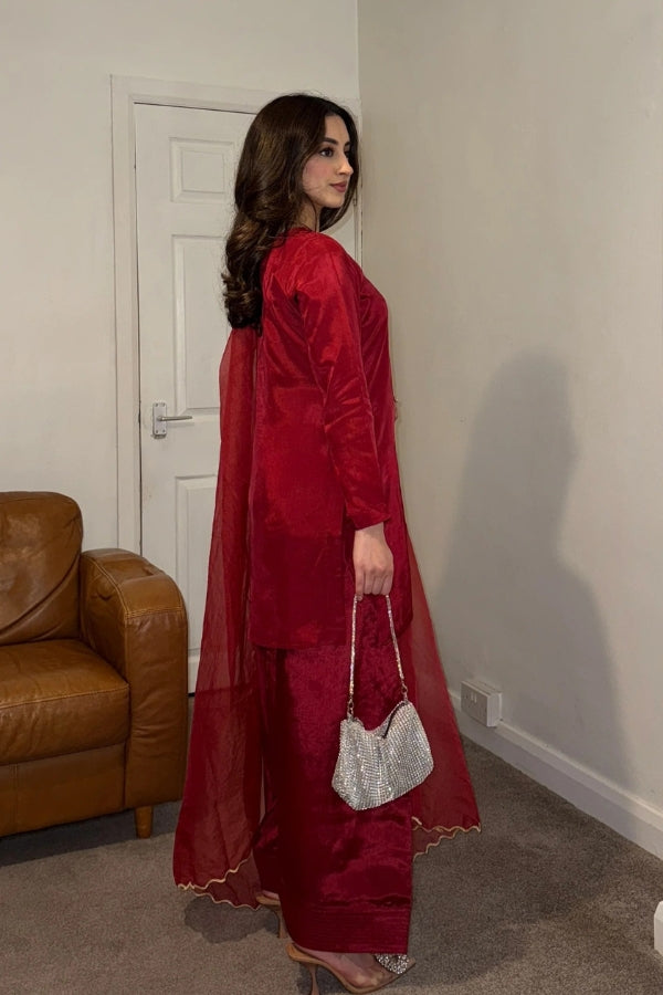Woman in a red traditional outfit holding a silver purse in a room with a brown leather couch.