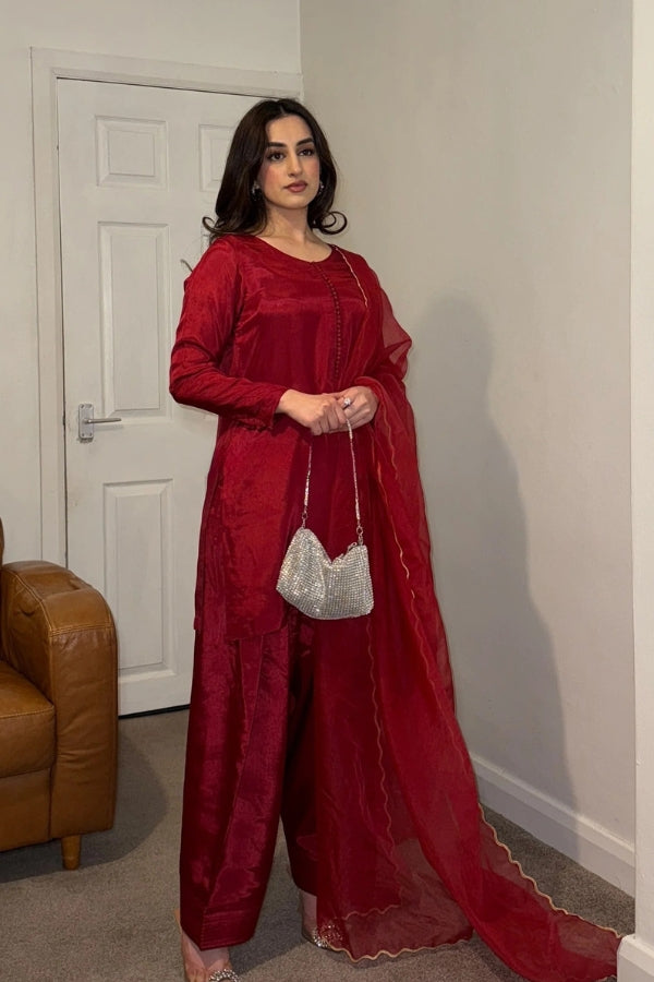 Woman in a red traditional outfit standing in a room with a white door and brown leather couch.