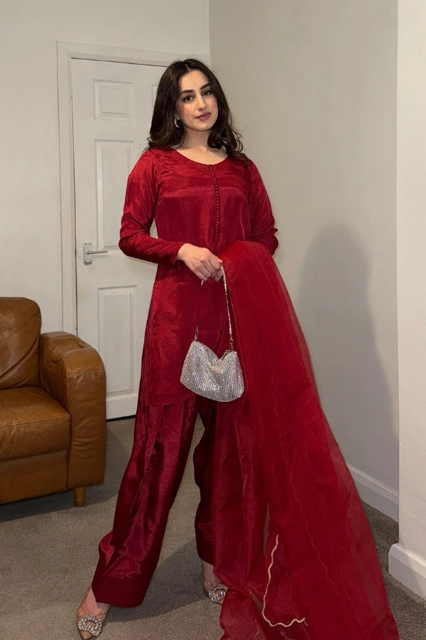 Woman in a red traditional outfit holding a silver purse in a room with a brown couch.