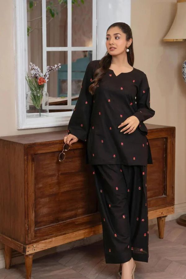 Woman in a black outfit with red patterns standing next to a wooden cabinet.