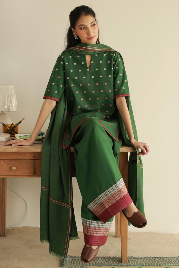 Woman wearing a green traditional outfit with a matching dupatta, sitting on a stool.