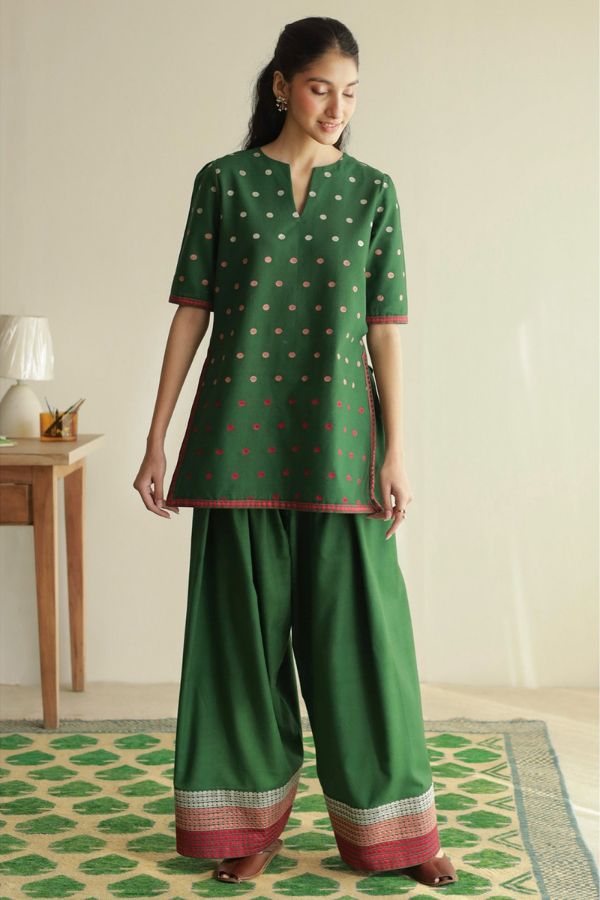 Woman wearing a green traditional outfit with a patterned top and wide-leg pants in a room.