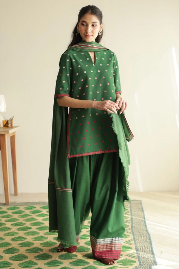 Woman wearing a green traditional outfit with a matching dupatta in a room.