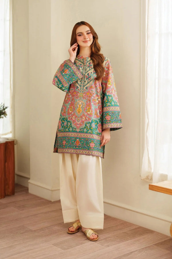 Woman wearing a colorful embroidered top and white pants indoors.