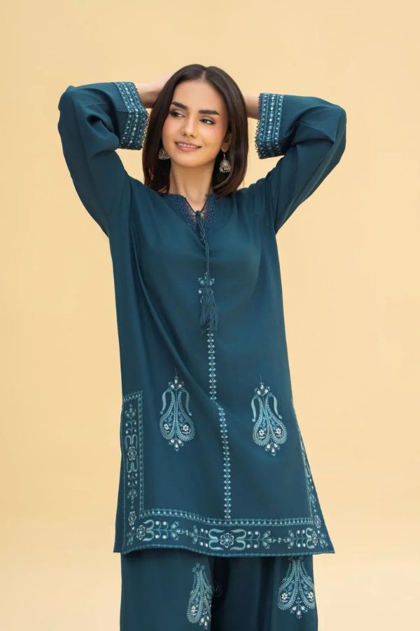 Woman wearing a teal embroidered outfit against a beige background