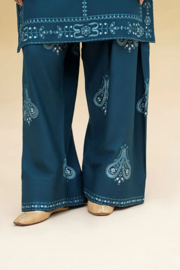 Teal embroidered outfit with pants and a top on a beige background