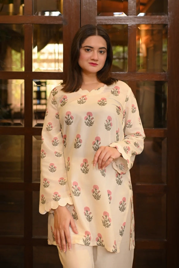 Woman wearing a light-colored floral blouse with white pants indoors.