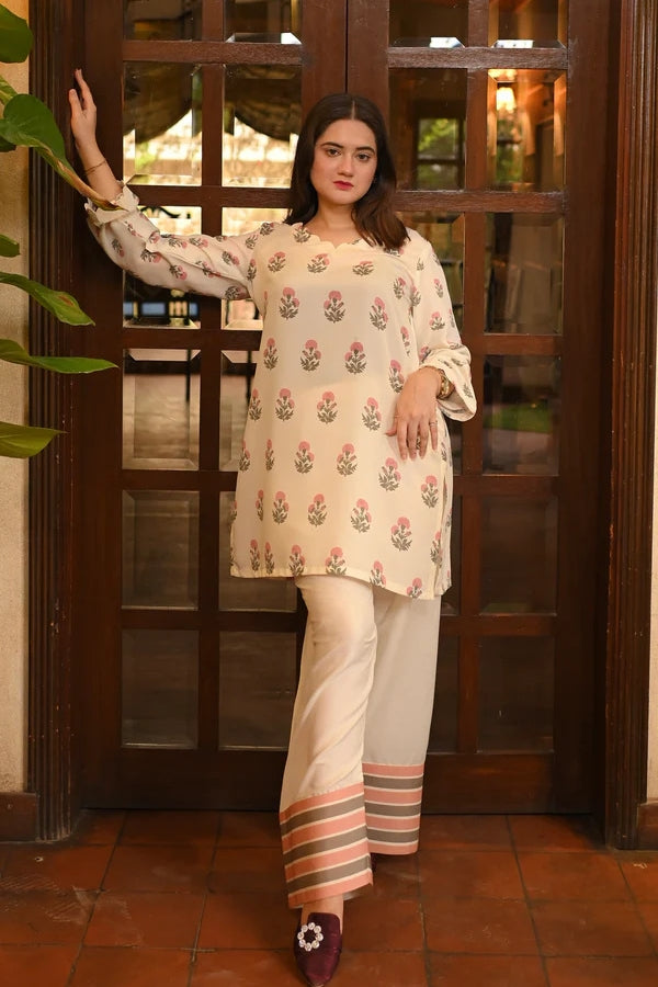 Woman in a floral top and white pants standing in front of a wooden door.