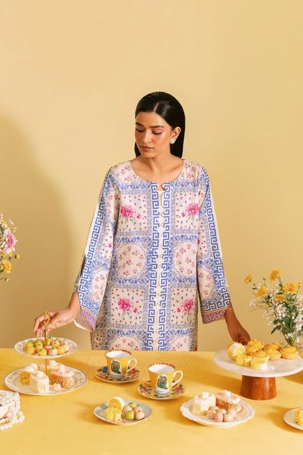 Woman in a patterned dress standing behind a table with tea set and snacks on a yellow background